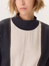 Remera blanca de manga larga con cuello alto, corte holgado y costuras verticales decorativas en el frente.