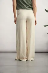 Pantalón de corte amplio y tiro alto, confeccionado en tela con textura tipo lino. Presenta un diseño envolvente en la cintura con un lazo lateral para anudar, creando un efecto de superposición frontal.