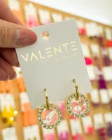 Aros colgantes con forma circular, con centro marmolado en tonos rosa y blanco, y borde con strass. El aro es de acero dorado.