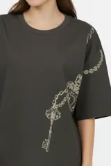 Remera oversize de algodón color gris oscuro, con cuello redondo, mangas cortas y estampado lateral en tonos claros de cadenas y una llave.