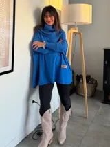 Polerón oversize de tejido de punto color naranja, con cuello alto tipo polera, mangas largas con puños acanalados y bolsillos laterales. Presenta un detalle de etiqueta de cuero en la parte inferior.