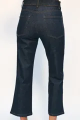 Jeans de tiro medio con corte cropped flare, confeccionados en denim azul oscuro. Presentan diseño de cinco bolsillos, trabillas en la cintura, raya planchada en el delantero y bajo con acabado evasé. Cierre frontal con cremallera y botón metálico.