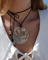 Collar con dije central de metal con forma de ostra irregular y texturizada, montado sobre un cordón de algodón negro ajustable que permite diversas formas de uso.