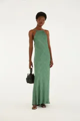 Vestido largo verde con estampado sutil de conchas marinas, escote halter y tirantes finos. Presenta un diseño fluido y silueta recta con escote en la espalda.