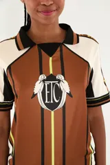 Camiseta deportiva estilo polo de color marrón con diseño estampado, cuello negro y detalles en blanco y verde flúor. Cuenta con mangas cortas y escudo frontal con las iniciales 'ETC' flanqueadas por aves.