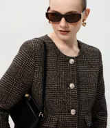 Casaqueto femenino de corte recto y largo corto, confeccionado en tejido estructurado con textura chevron. Presenta escote redondeado sin cuello, manga larga, cierre frontal con botones visibles y bolsillos decorativos con solapa.