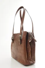 Cartera de hombro estructurada color negro, confeccionada en 100% cuero vacuno con textura en relieve tipo reptil. Cuenta con asas largas ajustables mediante hebillas metálicas plateadas, cierre superior y el logo de la marca grabado en la parte frontal.