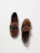 Mocasines de gamuza sintética color marrón, con detalle de pelo sintético en la parte superior y una tira de cuero sintético negro con hebilla metálica. Poseen un diseño de punta redondeada y taco bajo.
