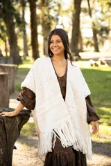 Ruana de lana merino color crudo, con diseño tejido de textura en relieve y terminación con flecos largos en el ruedo.