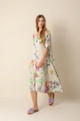 Vestido largo estampado con flores en tonos violeta, naranja, verde y azul sobre un fondo beige claro. Tiene cuello en V y mangas cortas.