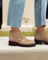 Botín corto de cuero color visón (beige/topo), con cierre de tres tiras de velcro en el empeine. Posee cuello acolchado de gamuza y suela de goma negra con relieve tractor.