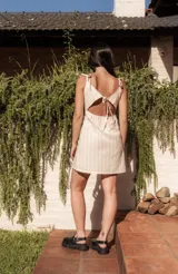 Minivestido beige con rayas verticales y bordados. Tiene breteles finos, escote recto con lazo ajustable, espalda elastizada y tajos laterales en el ruedo.