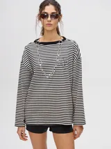 Remera manga larga a rayas horizontales grises y blancas, con cuello redondo rojo y logo bordado en el pecho. Corte holgado.