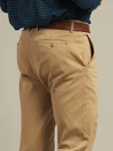 Pantalón de vestir color beige, de corte recto, con bolsillos laterales y traseros. Se ajusta a la cintura con cinturón de cuero marrón.