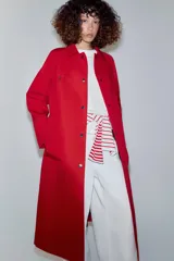 Trench largo color rojo de la línea ZW Collection de Zara, con cuello solapa, manga larga y bolsillos laterales ocultos. Presenta un diseño con forro interior a contraste y cierre frontal con botones a presión.