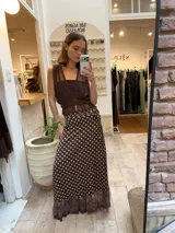 Pollera midi tipo pareo de satén color chocolate con estampado de lunares blancos. Presenta un diseño envolvente con ajuste lateral y un ruedo con detalle de microtul y puntilla bordada.