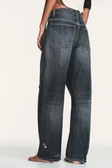 Jeans de tiro medio con diseño baggy balloon, cinco bolsillos y costuras laterales torcidas. Presenta un acabado desgastado con roturas localizadas y cierre frontal con cremallera y botón metálico.