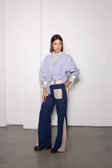 Camisa de manga larga con diseño combinado en tres telas, presentando un patrón de rayas verticales en azul y blanco. Cuenta con cuello alto, volados frontales y puños en contraste. El diseño es holgado con mangas abullonadas.