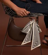 Cartera baguette pequeña de material sintético color marrón, sin estampa, con correa de mano y cierre de cremallera. No incluye pañuelo.