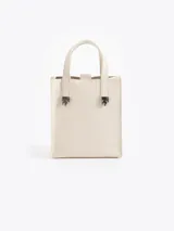 Cartera tipo tote de tamaño pequeño, color crema, con diseño estructurado y minimalista. Presenta asas fijas con herrajes metálicos decorativos en forma de llama en la base de las mismas.