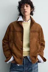 Cazadora de piel con acabado ante color marrón, corte relaxed fit, cuello bowling y manga larga con puño abotonado. Presenta bolsillos de vivo en la cadera y cierre frontal de botonadura.