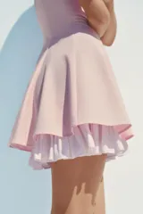 Vestido corto color rosado pálido, con escote cuadrado y tirantes finos ajustables. El bajo tiene un forro con volado de tela a rayas verticales blancas y rosadas.
