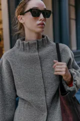 Chaqueta estilo bomber de punto color gris, con cuello subido, manga larga y acabados elásticos con frunces en puños y cuello. Cierre frontal con botones a presión ocultos.