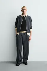 Pantalón jogger de corte wide fit en tejido compacto color gris oscuro. Presenta cintura elástica con cordón ajustable, bandas laterales en contraste color beige y costuras frontales tipo pinza.