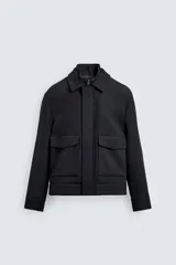 Cazadora de corte regular fit en color negro. Presenta cuello solapa con un cuello interior de punto desmontable mediante cremallera. Cuenta con cierre frontal de cremallera oculta por una solapa con botones a presión, bolsillos de plastrón con solapa en la cadera y mangas largas con puños abotonados.