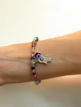 Pulsera elástica compuesta por cuentas de cristal multicolor y abalorios de ojos turcos, con dije colgante de mano de Fátima decorado con cristales y un ojo turco adicional.
