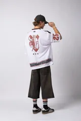 Camiseta blanca de poliéster con cuello en V negro y ribete rojo. Estampado frontal con una estrella negra y texto con efecto desgastado. Mangas cortas con números '0' y '1' en color rojo.