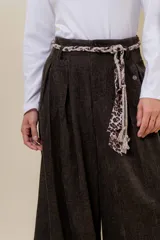 Pantalón wide leg de tiro alto en color negro, con diseño de pinzas delanteras que aportan volumen y caída fluida. Incluye bolsillos laterales y un lazo desmontable en la cintura que combina cordón con cinta de estampado animal print.