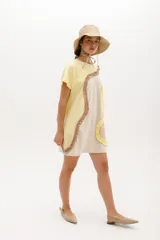 Vestido corto de algodón con diseño de bloques de color en tonos azul y celeste. Presenta un corte relajado, cuello redondo, mangas cortas y detalles de volados aplicados en forma curva a lo largo de la prenda.