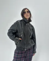 Campera bomber de cuero negro con efecto desgastado en las costuras, diseño oversize, cuello alto, bolsillos frontales con solapa y cierre frontal con botones a presión.