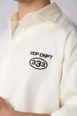 Camisa de manga corta negra, de corte boxy, con cuello camisero, cierre frontal de botones y bordado circular en el pecho.