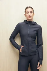 Campera deportiva negra de calce entallado, con cierre frontal completo, capucha integrada y mangas largas con puños envolventes. Presenta costuras estratégicas que estilizan la silueta y bolsillos laterales funcionales.