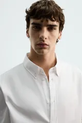 Camisa de corte regular fit confeccionada en tejido de algodón con textura. Presenta cuello abotonado, manga larga con puños abotonados y cierre frontal con botones.