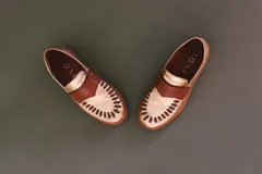 Mocasines de cuero en color dorado con detalles en marrón, con diseño bicolor y costuras artesanales expuestas en el empeine.