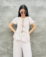 Blusa estampada con hojas verdes y blancas, con escote en V y mangas cortas abullonadas. Presenta volados en el ruedo y detalle de lazos en el frente.