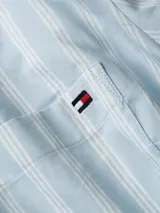 Camisa de manga larga Tommy Hilfiger confeccionada en popelina de algodón, con diseño de rayas verticales en tonos azul claro y blanco. Presenta cuello camisero clásico, cierre frontal con botones y un bolsillo de parche en el pecho con el logo de la marca bordado.