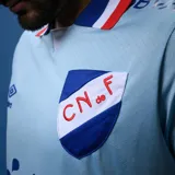 Camiseta de fútbol Umbro del Club Nacional de Football, modelo Away 3. Diseño celeste con detalles en azul y rojo en cuello y mangas. Incluye logo de Umbro, escudo del club y sponsor Antel en el frente.