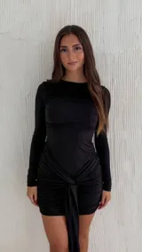 Vestido corto negro de manga larga, con escote redondo, diseño ajustado al cuerpo y fruncidos con detalle de lazo colgante en la cintura.