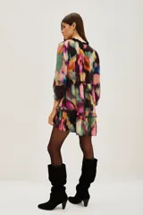 Vestido corto con estampado abstracto en tonos vibrantes como fucsia, verde, amarillo y negro. Presenta cuello con lazo ajustable y mangas largas abullonadas con puños elásticos. El cuerpo tiene un corte imperio con un volante fruncido en el ruedo.