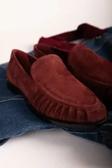 Mocasín de gamuza color bordó con detalle de frunces en la puntera y suela plana de goma negra.