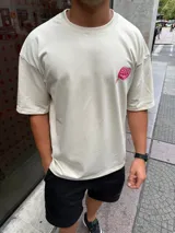 Remera de corte oversize color beige, con estampa gráfica en la espalda que representa un helado de palito derretido en color fucsia con la inscripción BHN y el texto Worldminded.