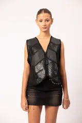 Chaleco negro de cuero artesanal con diseño de paneles combinados en cuero liso y cuero grabado con motivos florales. Presenta terminaciones en crochet, apliques calados en el bajo y cierre frontal con dije de borla.