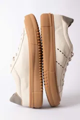 Championes urbanos de cuero en color crema con suela de goma gruesa en tono caramelo. Presentan detalles de costuras decorativas en el lateral y un refuerzo en el talón en color gris.