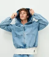 Campera bomber de jean en color azul medio, con cierre frontal de cremallera, capucha ajustable con cordones, bolsillos frontales y terminaciones elásticas en puños y cintura.