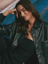 Sobrecamisa de cuero sintético en color negro, con cierre frontal de botones metálicos a presión, cuello clásico y un bolsillo frontal en el pecho.