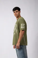 Remera de corte oversize color verde oliva con estampado frontal estilo universitario y detalles de líneas blancas en los hombros y laterales.